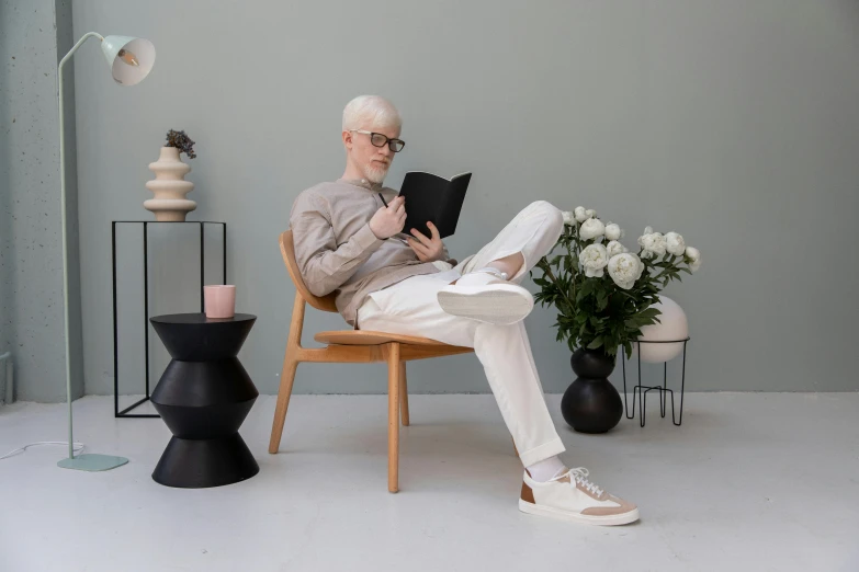 a man sitting in a chair reading a book, inspired by Graham Forsythe, pexels contest winner, aestheticism, wearing off - white style, scandinavian design, albino white pale skin, product introduction photo