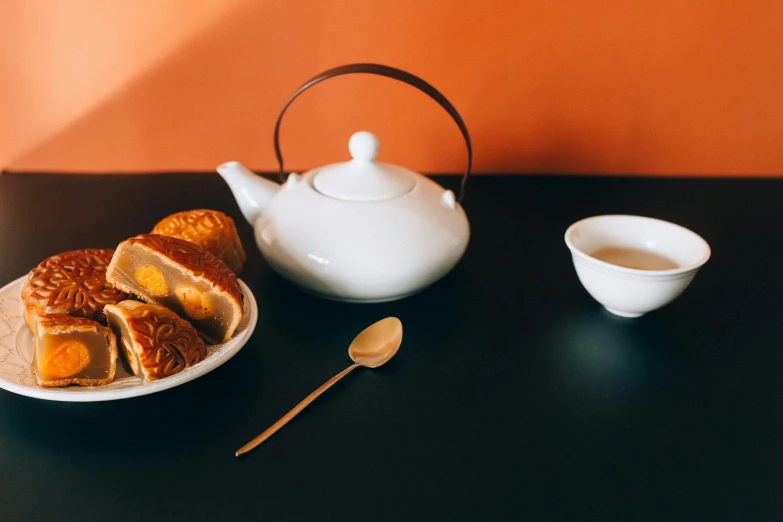 a white teapot sitting on top of a table next to a plate of food, a still life, inspired by Tōshi Yoshida, trending on unsplash, pastries, square, white and orange, dumplings on a plate