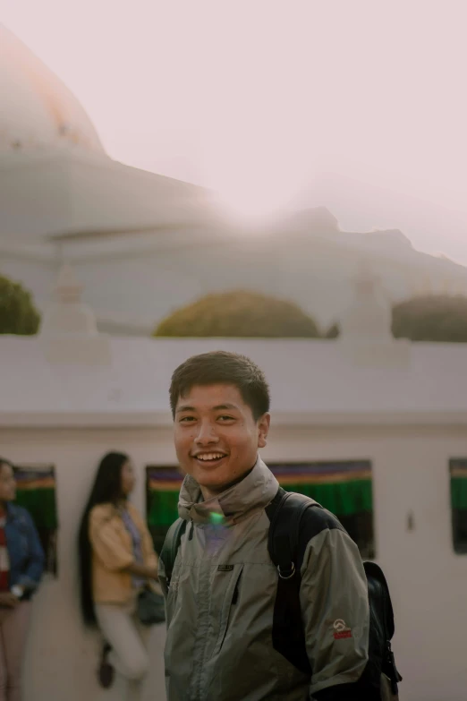 a man with a backpack standing in front of a building, a picture, inspired by Bian Jingzhao, happily smiling at the camera, glowing temple in the distance, profile image, explorer