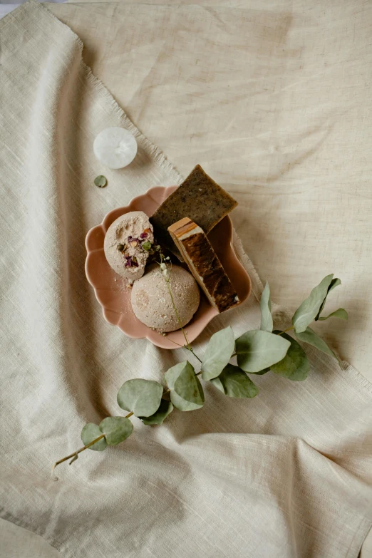 a close up of a plate of food on a bed, a still life, inspired by Eden Box, unsplash, renaissance, carved soap, brown and pink color scheme, cloth wraps, eucalyptus