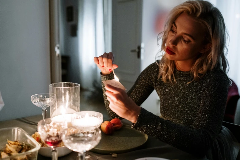 a woman sitting at a table with a fork in her hand, inspired by Elsa Bleda, trending on pexels, realism, candle lights, blonde swedish woman, drunk woman, ready to eat