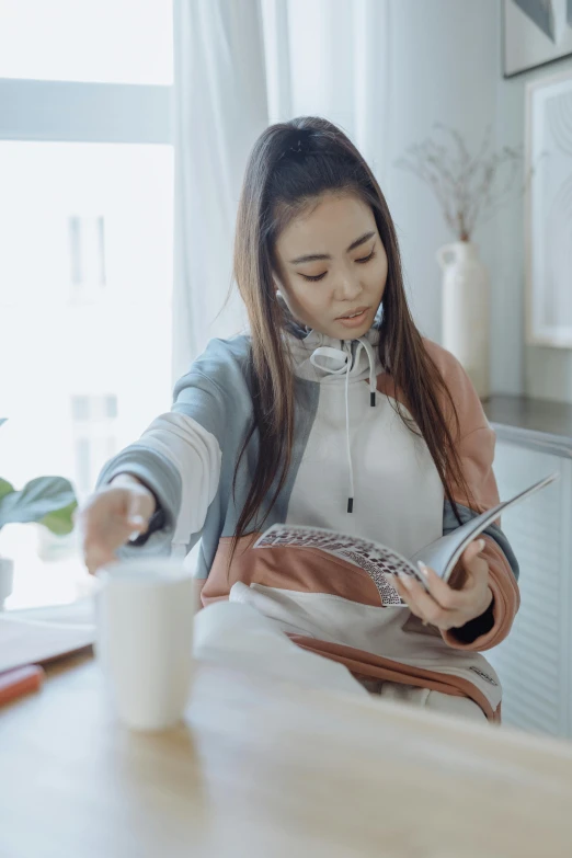 a woman sitting at a table reading a magazine, trending on pexels, happening, wearing a track suit, milk, a young asian woman, gif