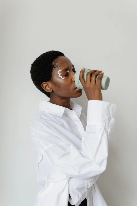 a woman in a white shirt drinking out of a cup, trending on pexels, afrofuturism, non binary model, grey skinned, ( ( dark skin ) ), skincare