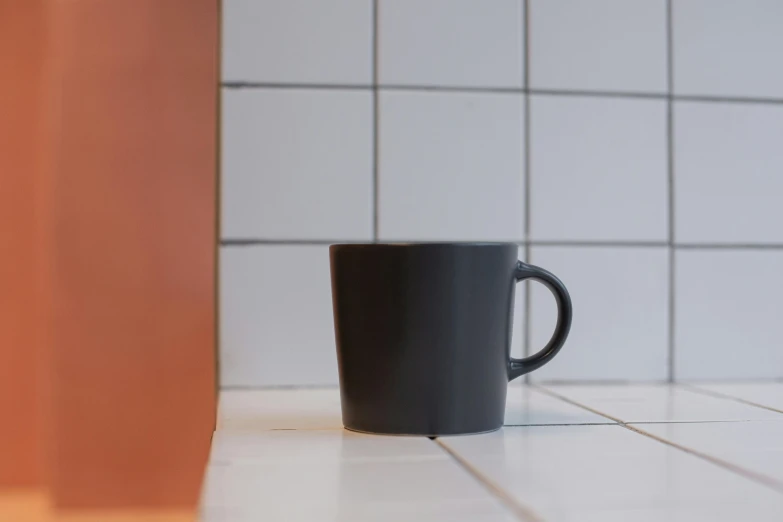 a black coffee cup sitting on top of a counter, by Niels Lergaard, grey, tiled, item, at an angle