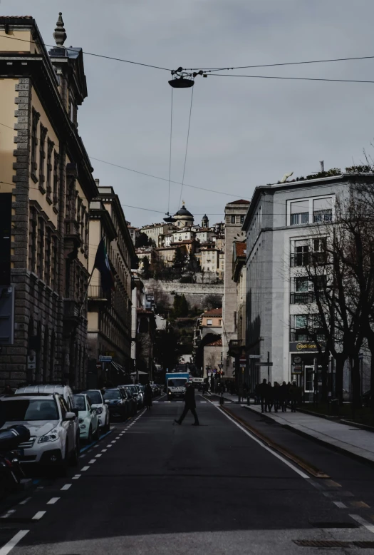 a man riding a bike down a street next to tall buildings, a picture, pexels contest winner, renaissance, castle on the mountain, khreschatyk, wires hanging above street, people walking around