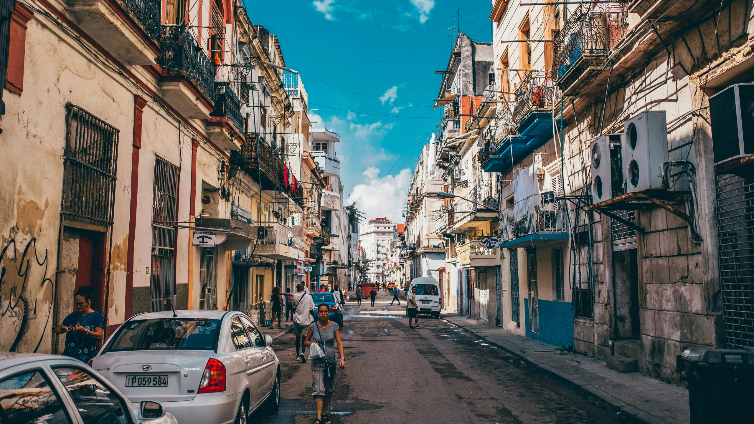 a narrow street lined with parked cars next to tall buildings, renaissance, cuban setting, people in the streets, top selection on unsplash, square