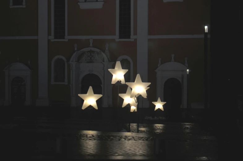 three lighted stars in front of a building at night, an ambient occlusion render, by Attila Meszlenyi, floor lamps, seven stars in right hand, inflateble shapes, church chandelier