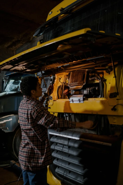 a man that is standing in front of a truck, by Dan Frazier, pexels contest winner, repairing the other one, yellow and black color scheme, in a workshop, nat geo