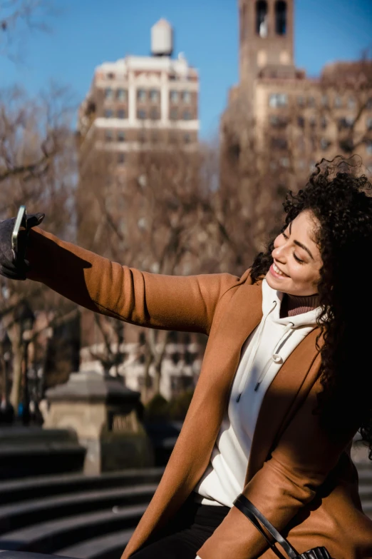 a woman riding a bike on a city street, trending on pexels, happening, taking a selfie, brown curly hair, wearing a turtleneck and jacket, arms stretched out