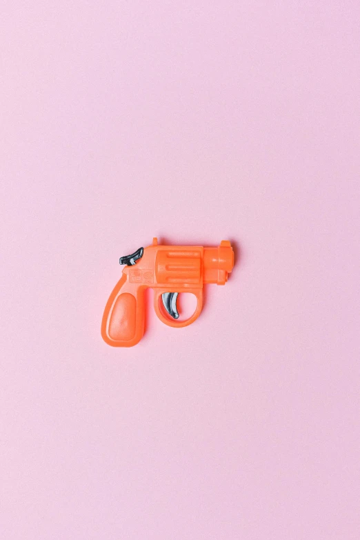 a toy gun sitting on top of a pink surface, inspired by Walther Jervolino, trending on pexels, pop art, orange skin, patricia piccinini, detailed trigger, candy