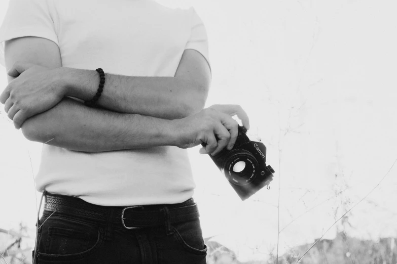 a black and white photo of a man holding a camera, a black and white photo, pexels contest winner, man in white t - shirt, minimal. sharp focus, cute photograph, hand on hip