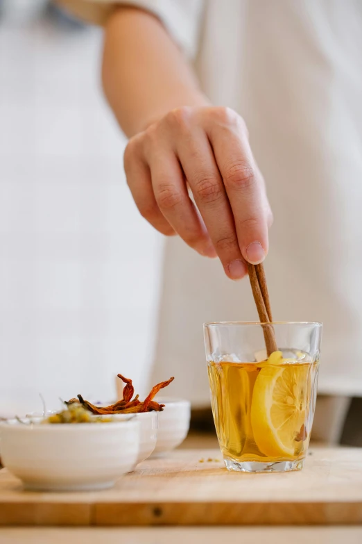 a person holding a wooden spoon over a bowl of food, a still life, inspired by Kanō Shōsenin, trending on pexels, process art, iced tea glass, square, apothecary, lemon