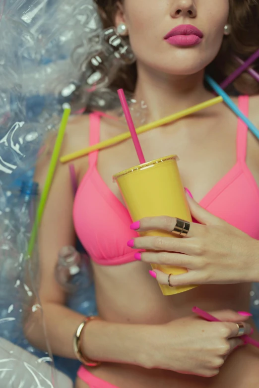 a woman in a pink bikini holding a plastic cup, by Julia Pishtar, trending on pexels, plasticien, neon tube jewelry, yellow, made of drink, gold bra