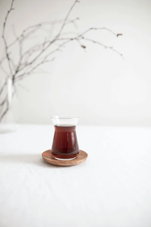 a cup of tea sitting on top of a saucer, by Yerkaland, unsplash, hurufiyya, in a short round glass vase, on a wooden plate, full body in shot, made of glazed