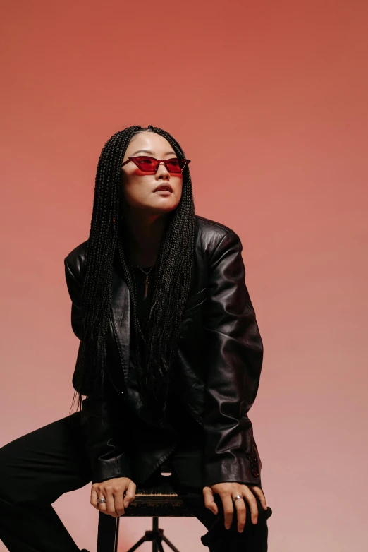 a woman sitting on top of a stool, an album cover, inspired by Zhu Da, trending on pexels, red sunglasses, long braided black hair, woman in streetwear, profile image