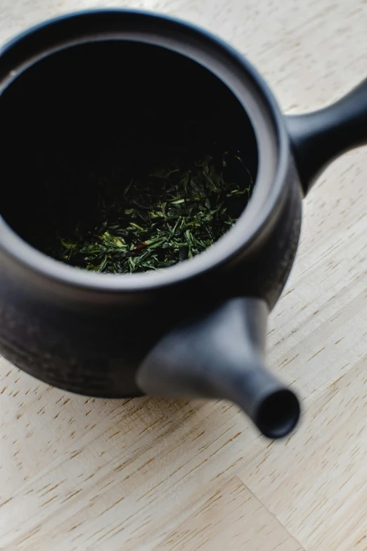 a black tea pot sitting on top of a wooden table, unsplash, mingei, herbs, detailed product image, high resolution image, green