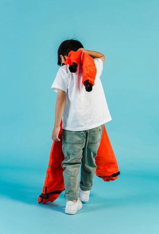 a little boy standing in front of a blue background, red fox, future inflatable jacket, pony facing away, wearing orange prison jumpsuit