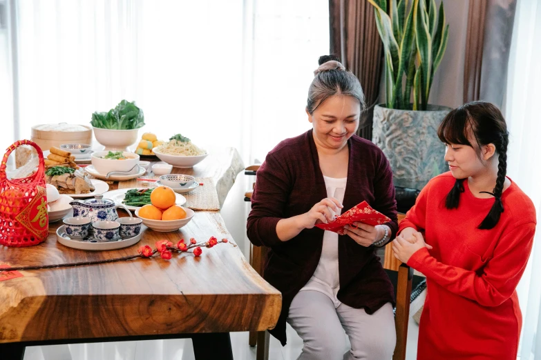 a couple of women standing next to each other at a table, pexels contest winner, hurufiyya, wearing a red cheongsam, ingredients on the table, profile image, an elderly