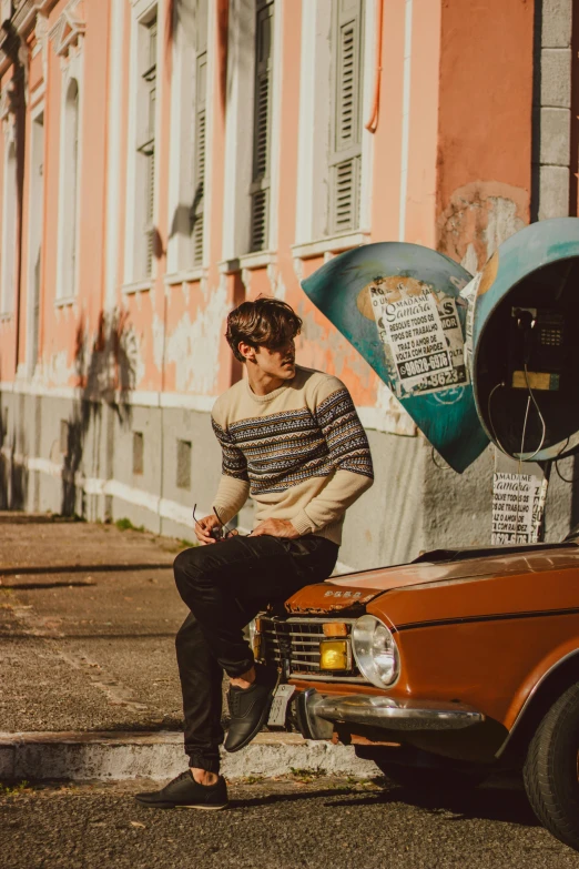 a man sitting on the hood of a car, an album cover, inspired by Luca Zontini, pexels contest winner, striped sweater, profile image, lisbon, caspar david