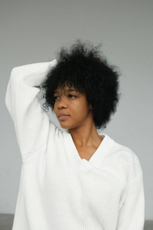 a woman wearing a white sweater and black pants, an album cover, by Lily Delissa Joseph, her hair is natural disheveled, looking away from camera, head and shoulders view, press shot