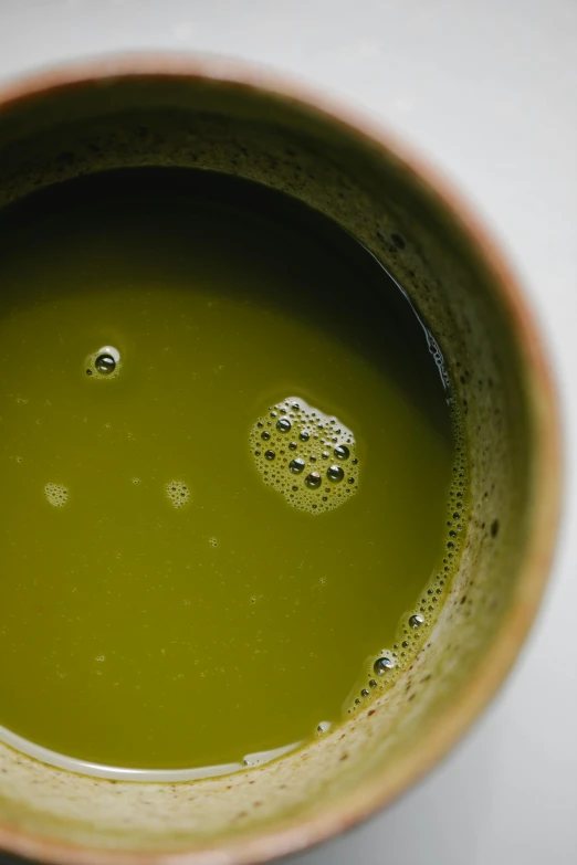 a close up of a cup of green tea, unsplash, inside dark oil, detailed product image, moringa juice, battered