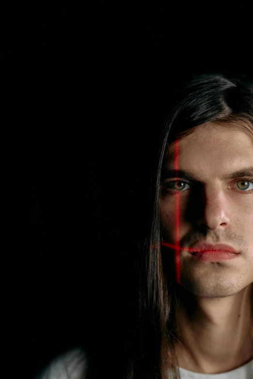 a man with long hair standing in front of a black background, flickr, conceptual art, symmetrical face orelsan, red contact lenses, video still, photographed for reuters
