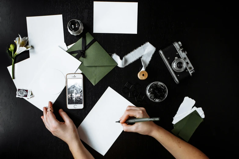 a person writing on a piece of paper, a black and white photo, by Julia Pishtar, pexels contest winner, knolling, card template, green and black color scheme, smartphone photo