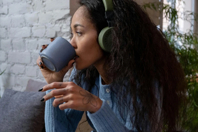 a woman sitting on a couch drinking a cup of coffee, trending on pexels, headphones dj rave, dipped in polished blue ceramic, #green, profile close-up view