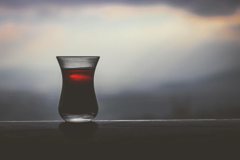 a glass filled with liquid sitting on top of a window sill, pexels contest winner, hurufiyya, mixture turkish and russian, maroon mist, nightcap, in a sunset haze