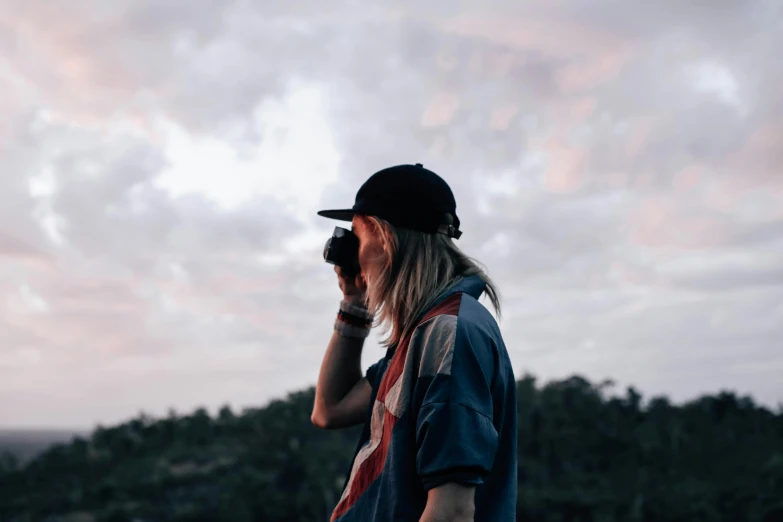 a man standing on top of a hill talking on a cell phone, pexels contest winner, wearing sunglasses and a cap, camera looking up at her, faded glow, casey cooke