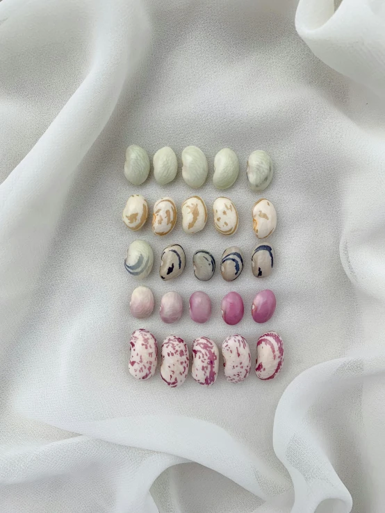 a bunch of beads sitting on top of a white cloth, a pastel, by Emma Andijewska, many cryogenic pods, covered with pink marzipan, marbling effect, flatlay