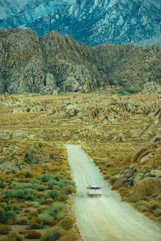 a car driving down a dirt road with mountains in the background, a picture, inspired by Wes Anderson, panfuturism, square, big rocks, ca, photograph from above