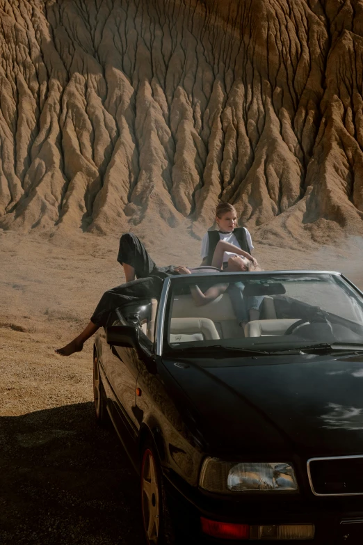 a couple of people sitting on top of a car, an album cover, unsplash, surrealism, chiseled formations, movie action still frame, sandworm, black car