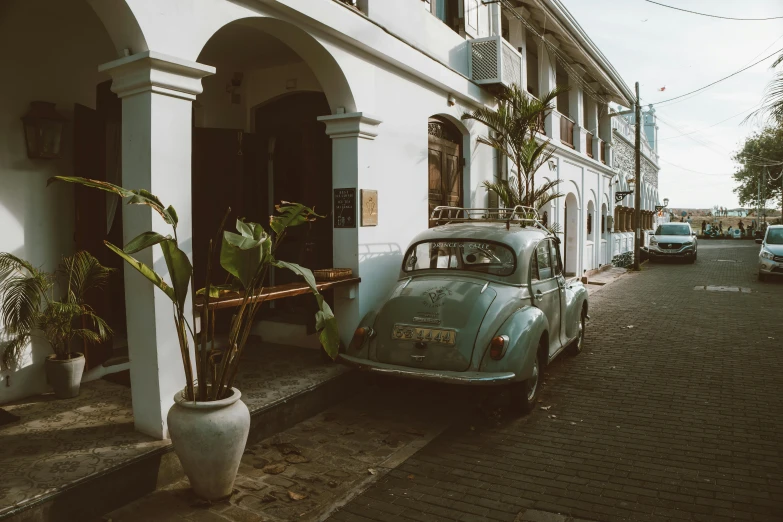 an old car parked in front of a building, by Daniel Lieske, pexels contest winner, with kerala motifs, hd footage, white and pale blue, cobblestone street