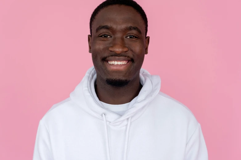 a man in a white hoodie smiles at the camera, inspired by Paul Georges, pexels contest winner, les nabis, wearing a pastel pink hoodie, ( ( dark skin ) ), blank background, jaylen brown
