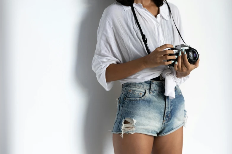 a woman in a white shirt is holding a camera, trending on pexels, wearing denim short shorts, at a fashion shoot, overexposure, medium format