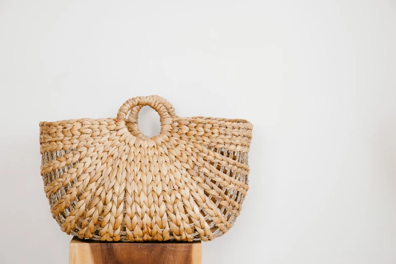 a straw bag sitting on top of a wooden block, by Andrée Ruellan, pexels contest winner, set against a white background, magnificent oval face, warmly lit, gypsy
