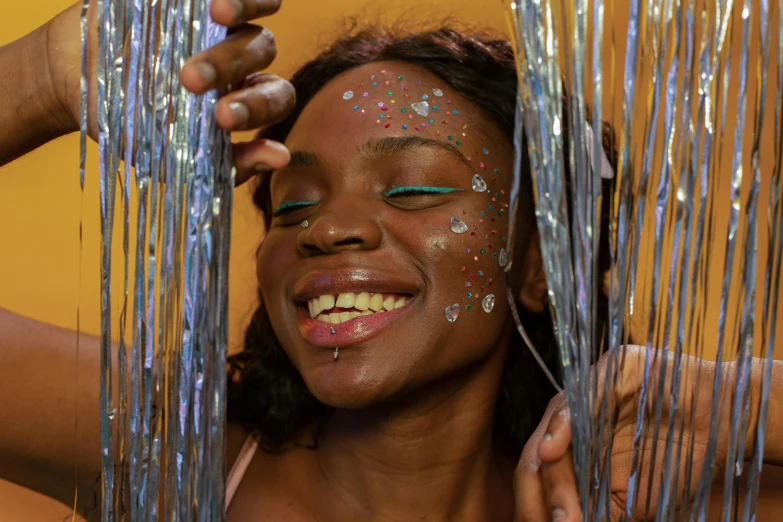 a close up of a person with glitter on their face, an album cover, by Jessie Alexandra Dick, trending on pexels, afrofuturism, smiling playfully, beaded curtains, elf with blue skin, photoshoot for skincare brand