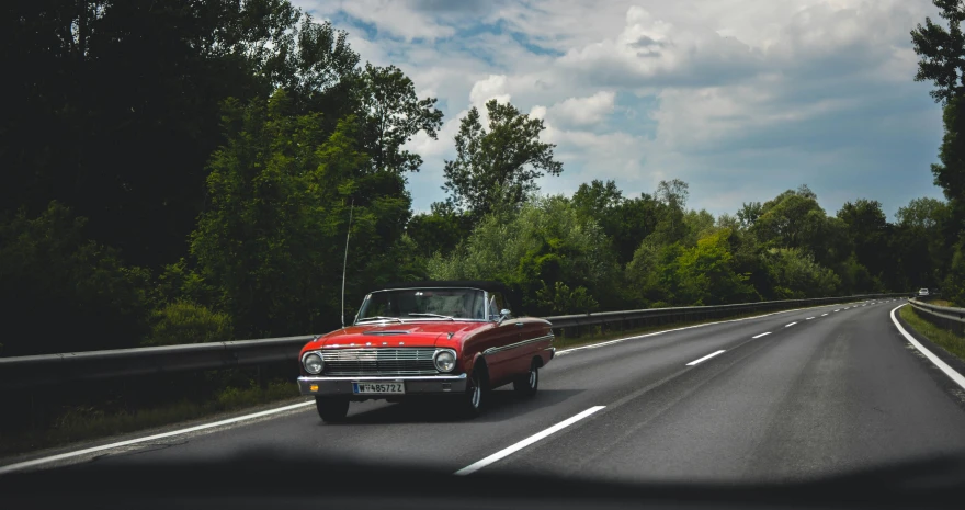 a red car driving down a road next to a forest, by Niko Henrichon, pexels contest winner, renaissance, mid-century modern, ford, car on highway, soft top