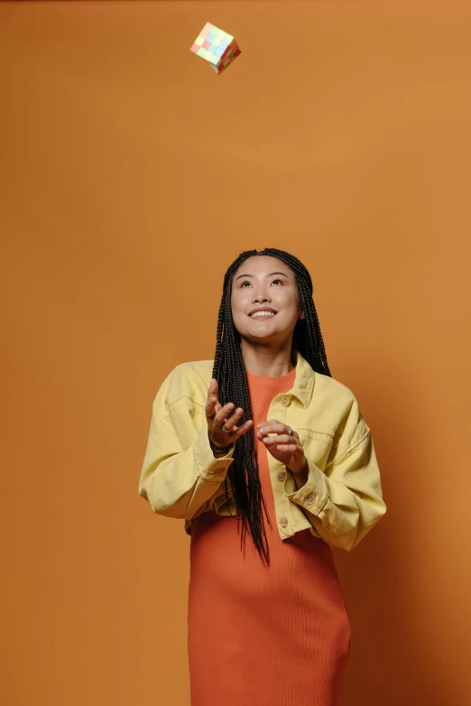 a woman in an orange dress standing in front of an orange wall, inspired by Kim Tschang Yeul, gestures, on a gray background, female with long black hair, ashteroth