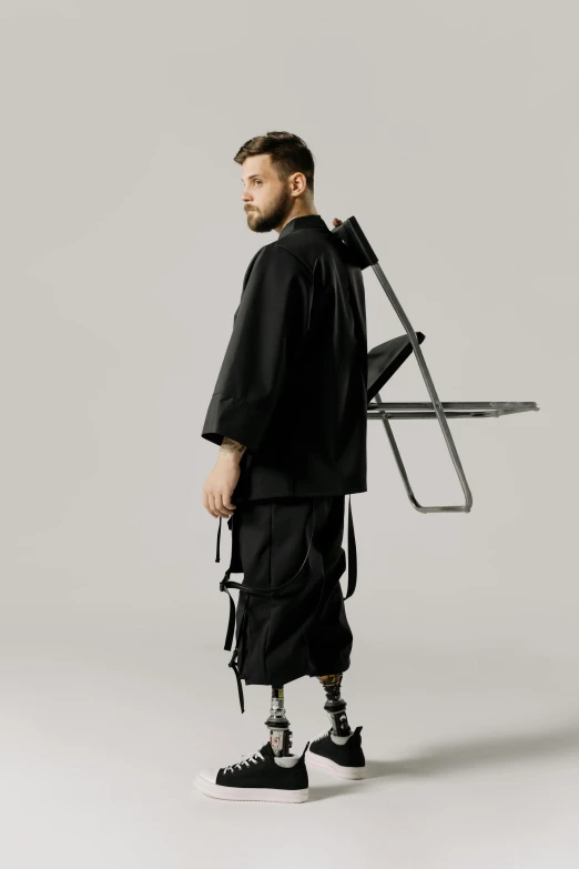 a man standing with a chair on his back, an album cover, inspired by Kuno Veeber, unsplash, neo-dada, wearing japanese techwear, wearing hakama, diverse medical cybersuits, zayn malik