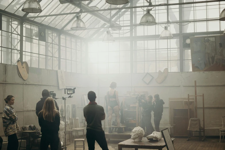 a group of people standing in a room, a matte painting, unsplash contest winner, visual art, light haze, in a factory, hammershøi, meet the actor behind the scenes