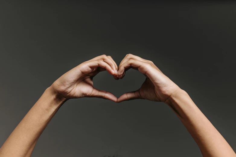 a woman making a heart with her hands, by Nina Hamnett, trending on pexels, hurufiyya, on a gray background, male and female, with a black background, high quality product image”