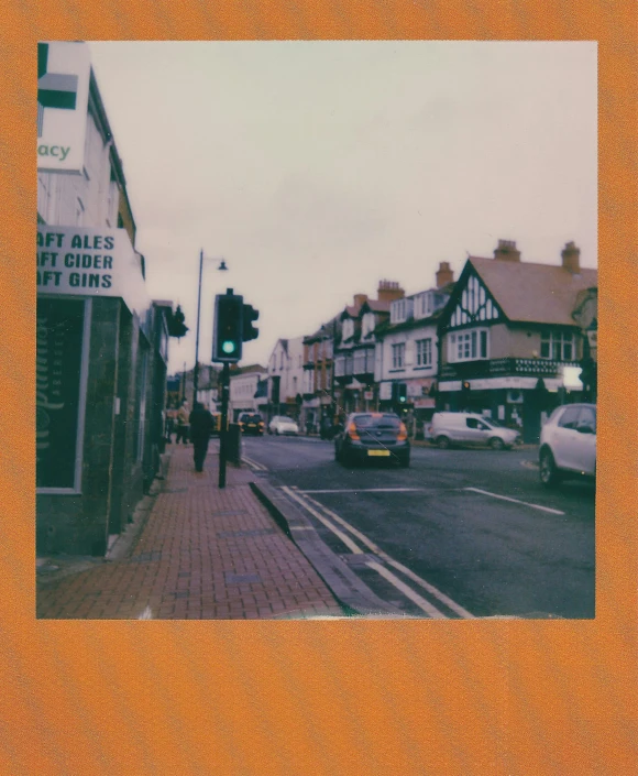 a street filled with lots of traffic next to tall buildings, a polaroid photo, by IAN SPRIGGS, unsplash, esher, orange tones, old shops, alternate album cover