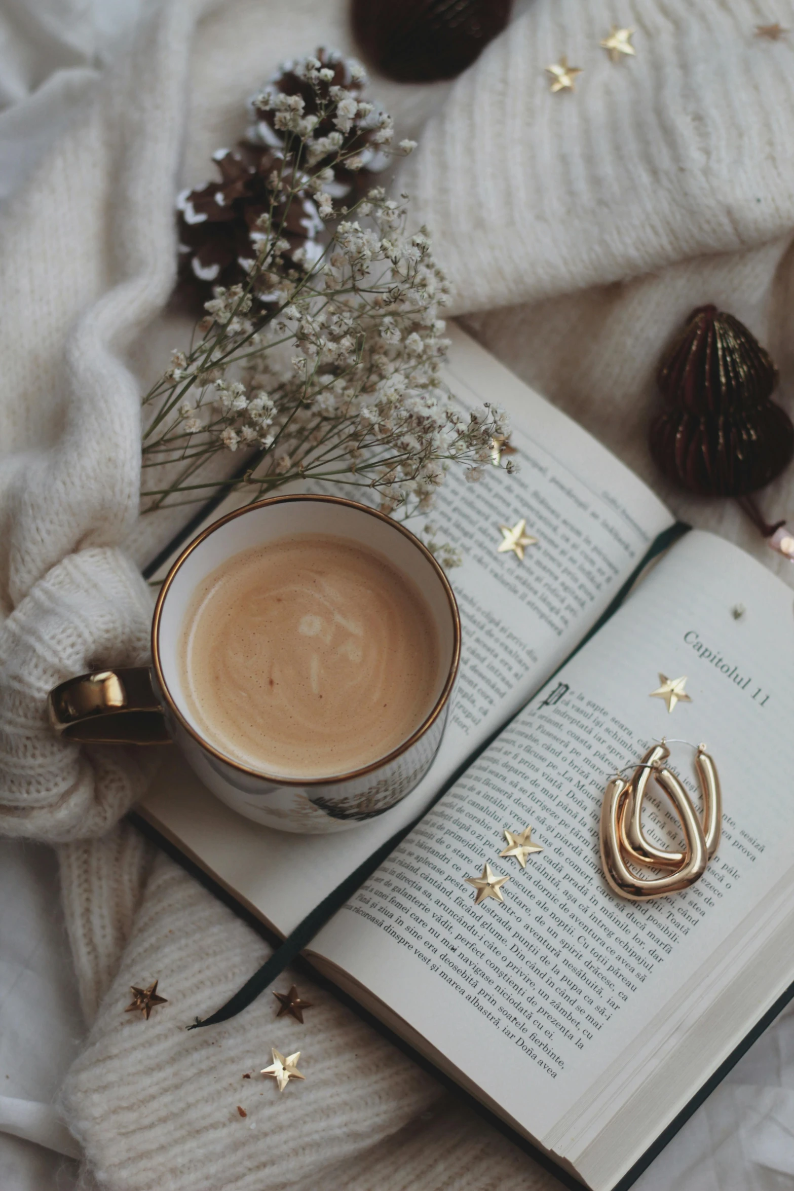 an open book sitting on top of a bed next to a cup of coffee, a still life, by Julia Pishtar, trending on pexels, gold earring, tiny stars, milk and mocha style, gold jewellery