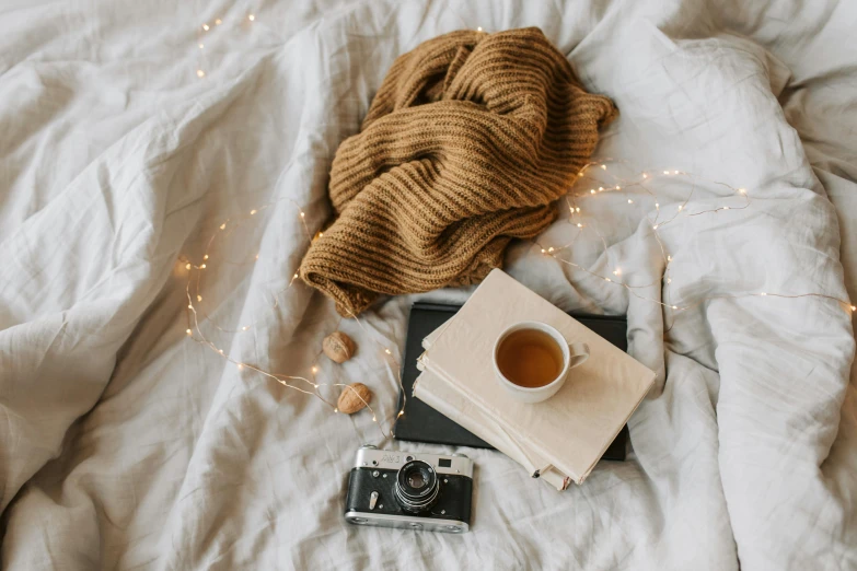 a blanket sitting on top of a bed next to a cup of coffee, a polaroid photo, by Julia Pishtar, trending on pexels, scattered props, brown sweater, tea drinking and paper lanterns, camera looking down upon