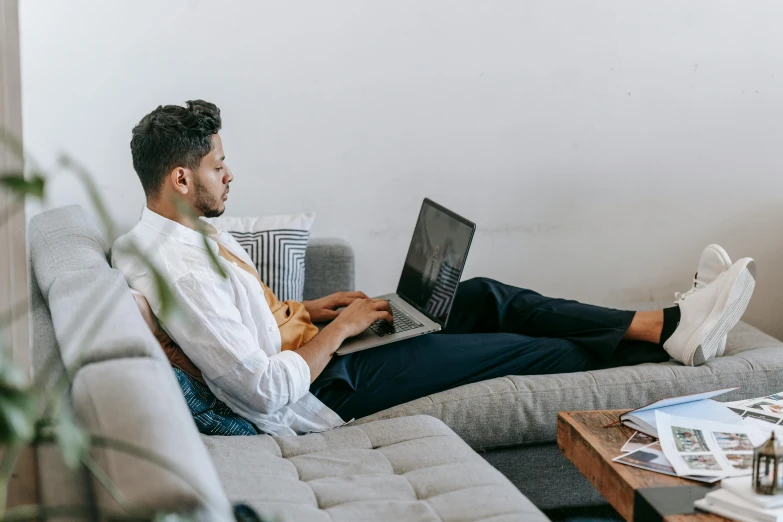 a man sitting on a couch using a laptop, trending on pexels, wearing business casual dress, raphael lecoste, facing sideways, guide