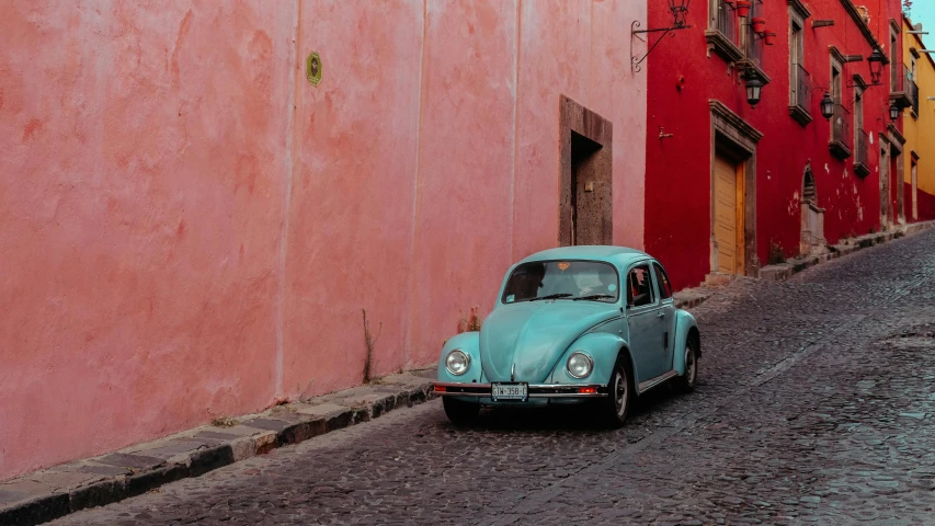 a car is parked on a cobblestone street, pexels contest winner, pink and teal color palette, beetle, mexican desert, red wall