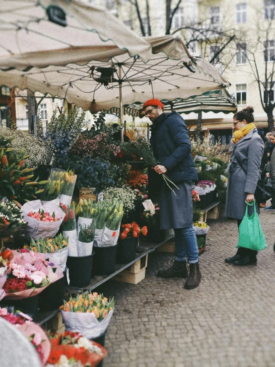 a couple of people standing in front of a bunch of flowers, by Niko Henrichon, trending on unsplash, renaissance, market stalls, 👰 🏇 ❌ 🍃, winter, shopping groceries