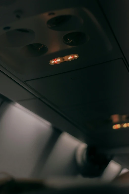 a close up of a person sitting in an airplane, lights on ceiling, panel of black, running lights, desaturated